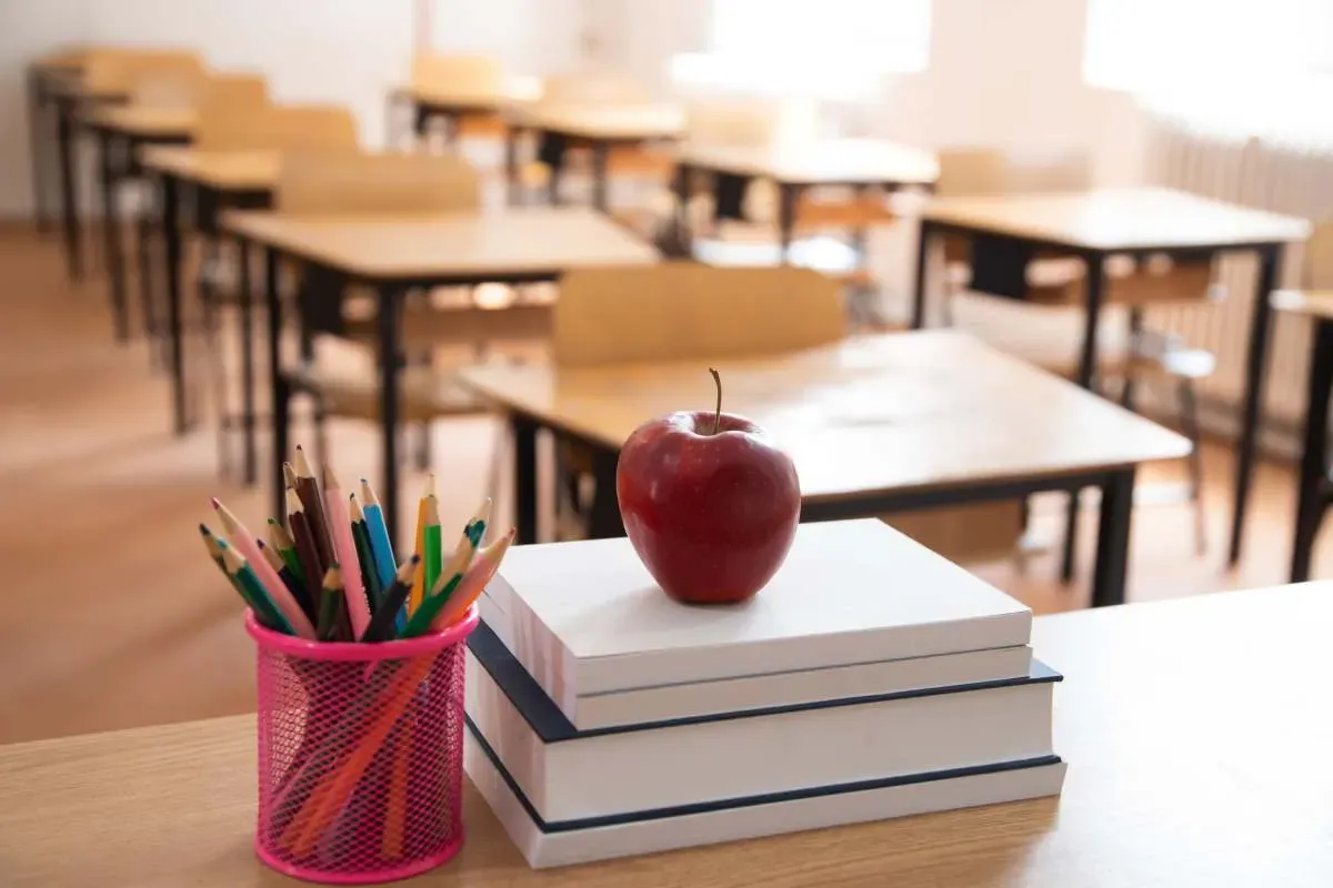 A classroom with a stack of books and a red apple on the desk