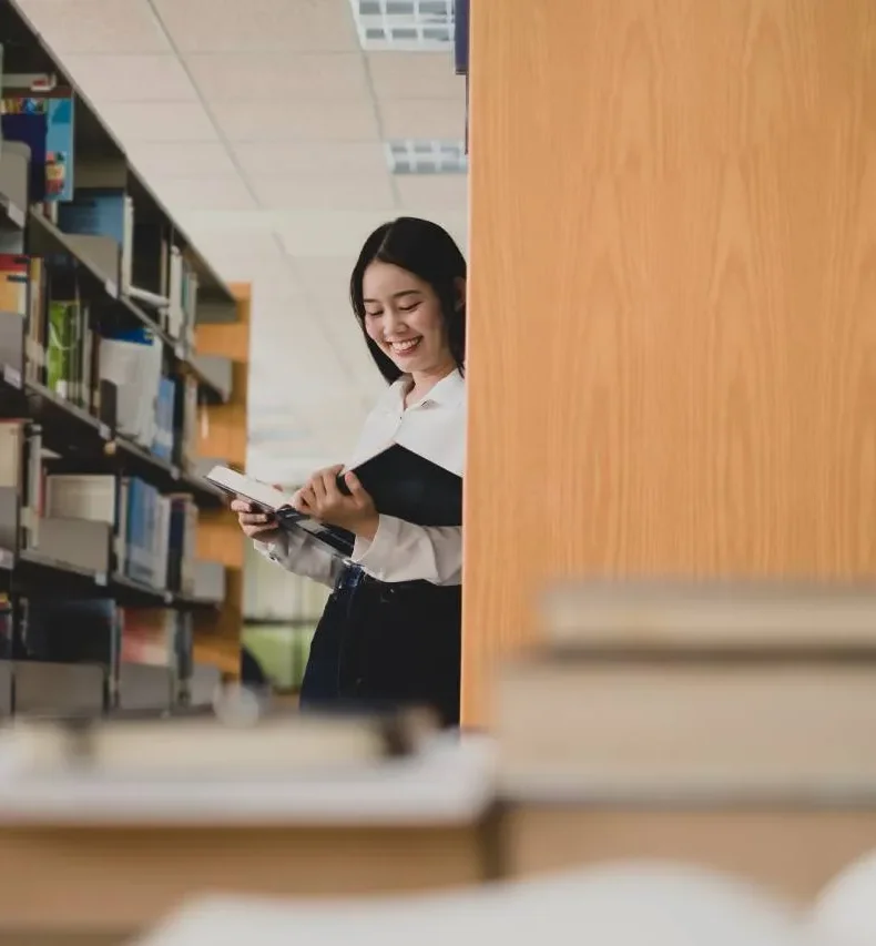 Học viên mỉm cười cầm sách trong thư viện